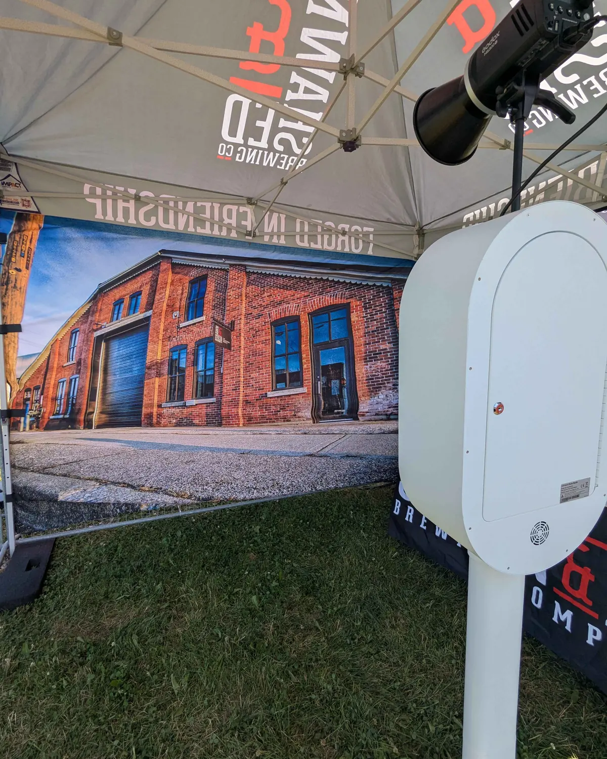 A custom-printed brick wall backdrop behind the Aura booth under a branded marquee at a festival