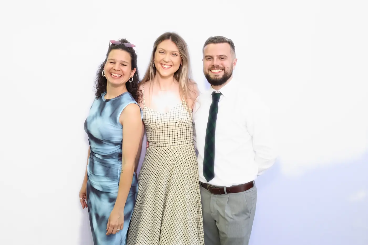 Three guests in formal wear posing together in the Aura photo booth